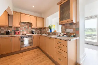 a kitchen with wooden cabinets and a large window at Popham Cottage in Cornwall in Newquay