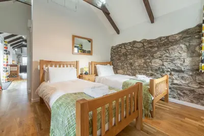 two beds in a room with a stone wall at Hunter's Barn in St. Agnes