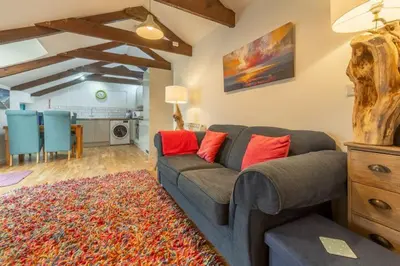 a living room with a gray couch and a kitchen at Potter's Barn in St. Agnes