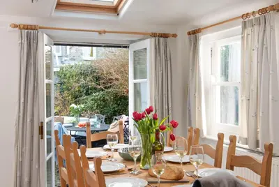 a dining room with a table with red flowers on it at Roseneath in St. Agnes