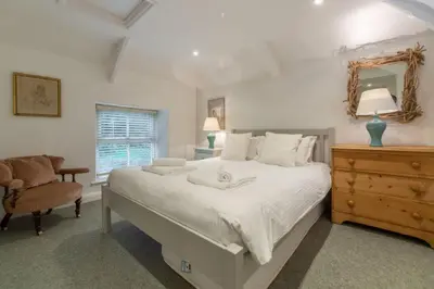 a bedroom with a bed and a chair and a mirror at Rose in Vale Cottage in Perranzabuloe