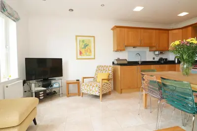 a living room with a kitchen and a table with chairs at Beachside apartment, sea views in St Merryn