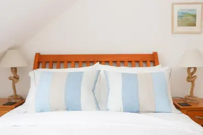 a bed with blue and white pillows and two lamps at Beachside apartment, sea views in St Merryn