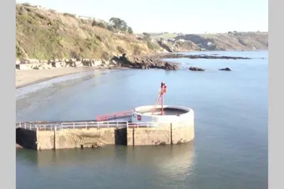 a boat in the water next to a beach at Millendreath at Westcliff - Self Catering flat with amazing sea views in Looe