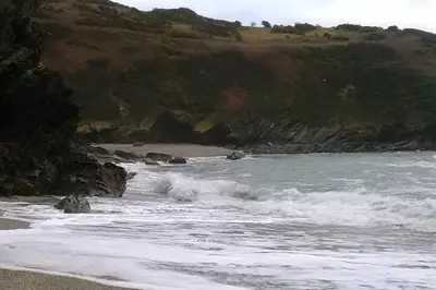 a beach with waves crashing on the shore at Millendreath at Westcliff - Self Catering flat with amazing sea views in Looe