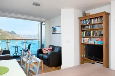 a living room with a couch and a book shelf at Millendreath at Westcliff - Self Catering flat with amazing sea views in Looe