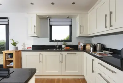 a kitchen with white cabinets and a black counter top at Sea Gem in St. Agnes