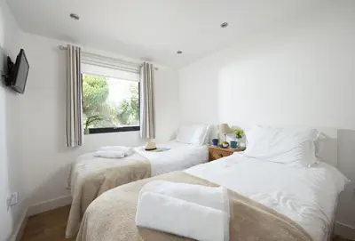 two beds in a white room with a window at Sea Gem in St. Agnes