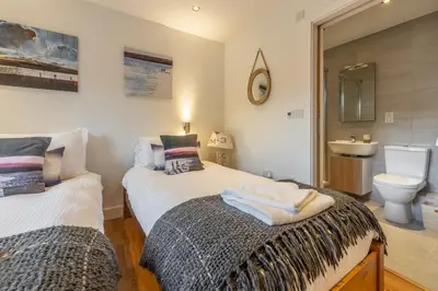 two beds in a room with a sink and a toilet at The Deck House in St. Agnes