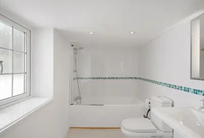 a white bathroom with a toilet and a bath tub at The Boy's Cottage in Portreath