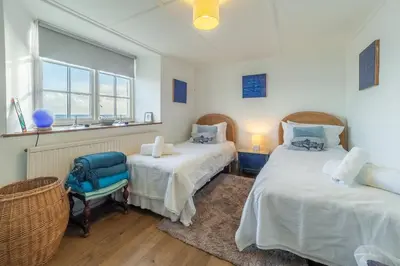 a room with two beds and a chair and a window at The Watch House in Helston