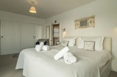 two beds in a bedroom with white sheets and pillows at The Watch House in Helston