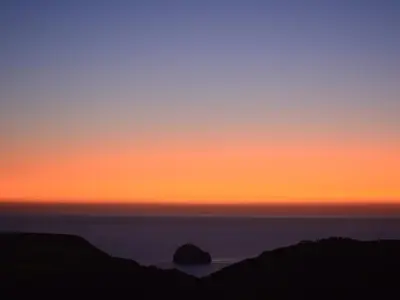 a sunset over the ocean with a rock in the water at Glenhaven in Tintagel