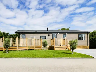 a manufactured home with a fence and a house at Pinehurst Lodge in Redruth