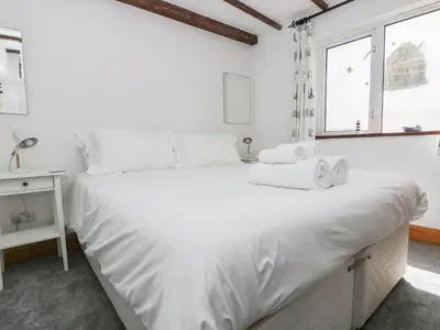 a white bedroom with a large white bed and a window at Polkirt Forge in Mevagissey