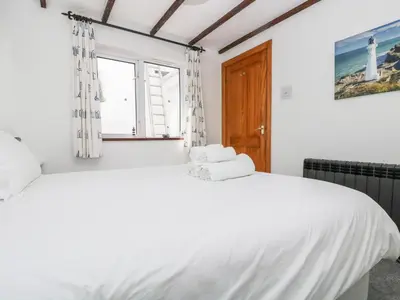 a white bedroom with two beds and a window at Polkirt Forge in Mevagissey
