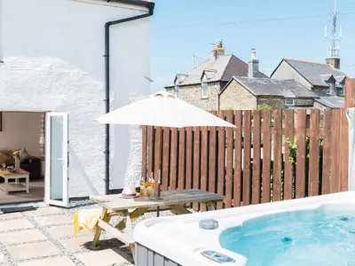 a hot tub on a patio with a table and an umbrella at Karrek in Tintagel
