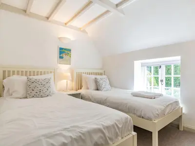 two beds in a bedroom with white walls and a window at 3 Rose Cottages in St. Agnes