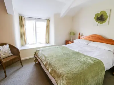 a bedroom with a bed and a window and a chair at 3 Rose Cottages in Looe