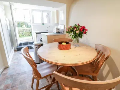a kitchen with a wooden table with chairs and a vase of flowers at 3 Rose Cottages in Looe
