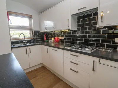 a kitchen with white cabinets and a black tile wall at Tremar in St Ives