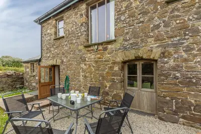 a patio with a table and chairs in front of a stone building at Spring Barn in Polzeath