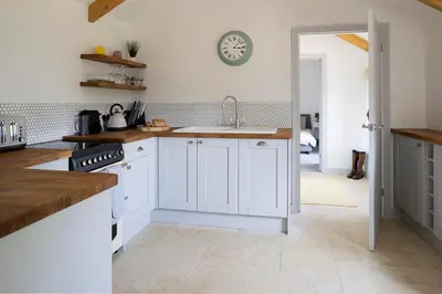 a kitchen with white cabinets and a clock on the wall at Cart Shed Cottage in Truro