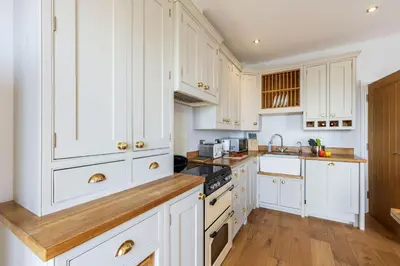 a white kitchen with white cabinets and wooden floors at 5 Fernhill in Carbis Bay