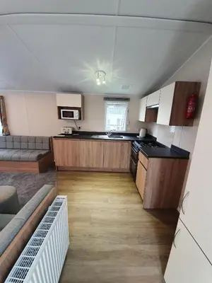 a kitchen with wooden cabinets and a couch in a room at Cozy 3 bedroom Caravan, Sleeps 8, at Parkdean Newquay Holiday Park in Newquay