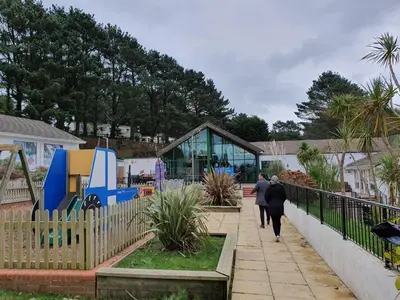 two people walking down a sidewalk next to a playground at Cozy 3 bedroom Caravan, Sleeps 8, at Parkdean Newquay Holiday Park in Newquay