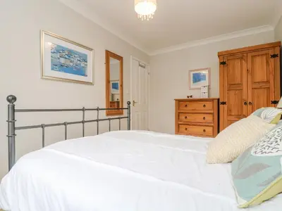 a bedroom with a white bed and a wooden dresser at Oyster Cottage in Falmouth