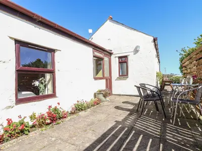 a patio of a white cottage with chairs and a table at Bowling Green Cottage in Redruth