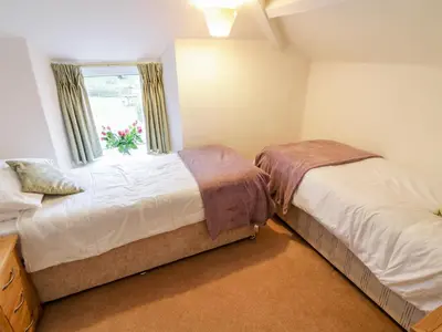 a bedroom with two beds and a window with flowers at 2 Rose Cottages in Looe
