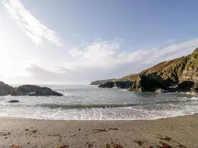 a sandy beach with rocks in the ocean at 2 Rose Cottages in Looe