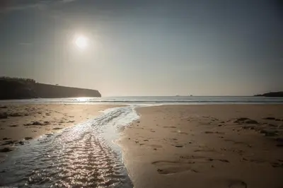 a beach with footprints in the sand and the ocean at APARTMENT BY THE BEACH, courtyard garden in St Merryn