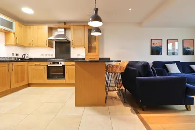 a kitchen with wooden cabinets and a bar with blue chairs at APARTMENT BY THE BEACH, courtyard garden in St Merryn