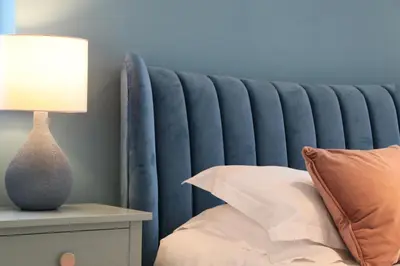 a bed with a blue headboard next to a table with a lamp at STYLISH, BEACHSIDE apartment, sea views in St Merryn