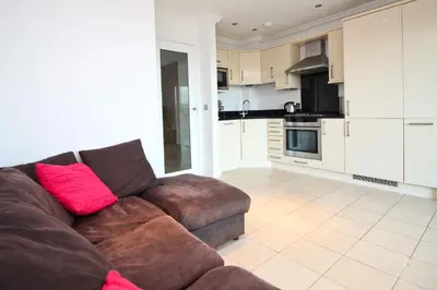 a living room with a brown couch and a kitchen at SEA VIEWS, beachside apartment with balcony in St Merryn