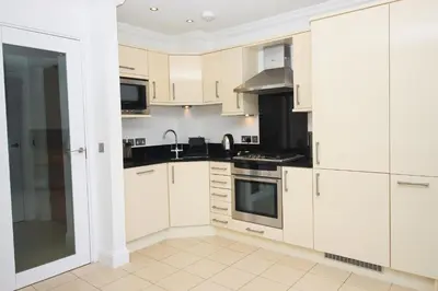 a kitchen with white cabinets and black appliances at SEA VIEWS, beachside apartment with balcony in St Merryn