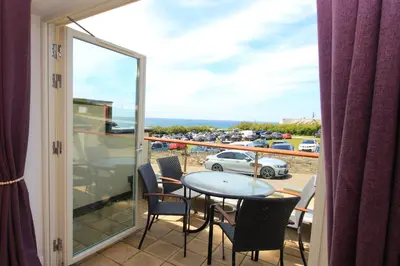 a balcony with a table and chairs and a view of a parking lot at SEA VIEWS, beachside apartment with balcony in St Merryn