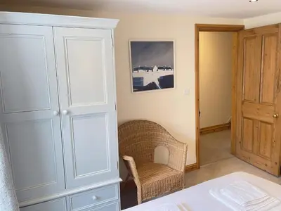 a bedroom with a white cabinet and a chair at Hollies Cottage in St Ives