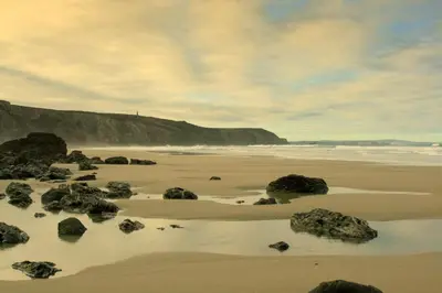 a sandy beach with rocks and the ocean at Tehidy Holiday Park Wigwam Camping Cabins in Illogan