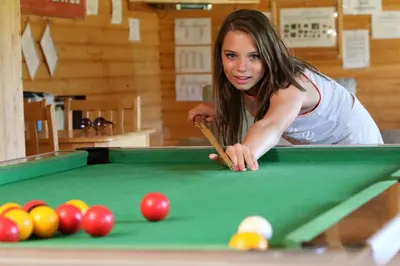 a woman playing pool with a cue on a pool table at Tehidy Holiday Park Wigwam Camping Cabins in Illogan