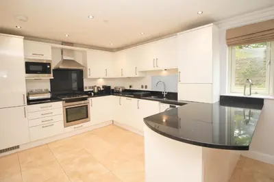 a kitchen with white cabinets and a black counter top at BEACHSIDE SPACIOUS apartment, private garden in St Merryn