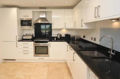 a kitchen with white cabinets and black counter tops at BEACHSIDE SPACIOUS apartment, private garden in St Merryn