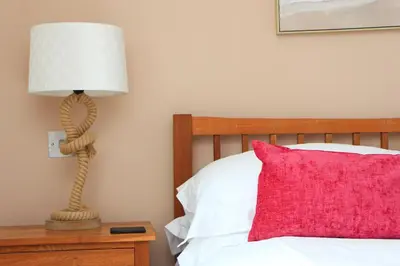 a bedroom with a bed with a lamp and a red pillow at BEACHSIDE SPACIOUS apartment, private garden in St Merryn