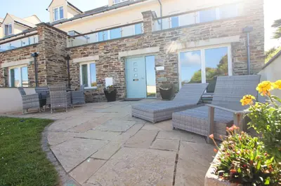 a patio with chairs and a table in front of a building at BEACHSIDE SPACIOUS apartment, private garden in St Merryn