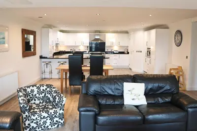 a living room with a leather couch and a kitchen at BY THE BEACH, spacious apartment in St Merryn