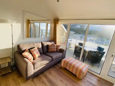 a living room with a couch and a large window at Sunsets In Porthtowan, Beachfront apartment in Porthtowan