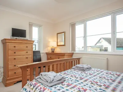 a bedroom with a bed and a dresser and windows at The White House in Poundstock